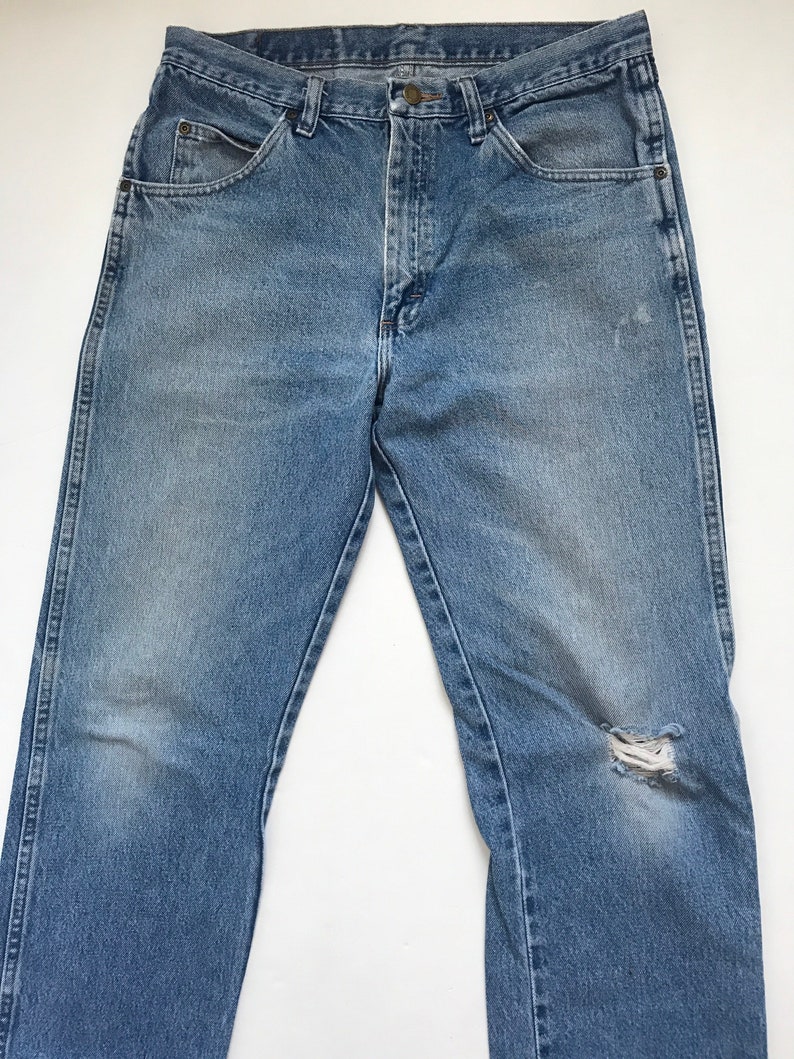 Pu&ograve; includere: Un paio di jeans in denim blu chiaro con un piccolo buco sul ginocchio destro.