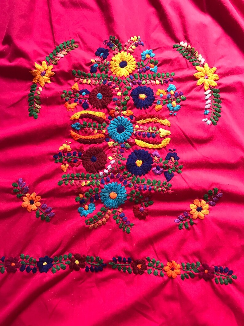 May include: A vibrant pink fabric with colourful embroidered flowers. The flowers are in shades of red, blue, yellow, green, and orange. The embroidery is detailed and intricate.