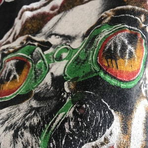 May include: Close-up of a black t-shirt with a white and green graphic print of a face wearing large green and red goggles. The text "JET DRO" is visible at the top of the image.