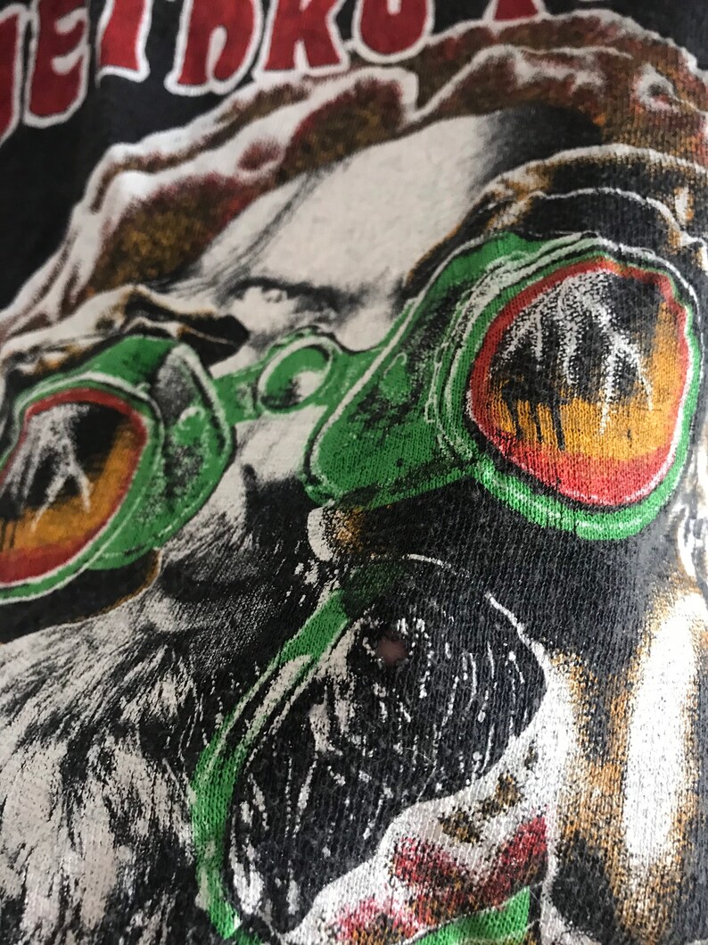 May include: Close-up of a black t-shirt with a white and green graphic print of a face wearing large green and red goggles. The text "JET DRO" is visible at the top of the image.