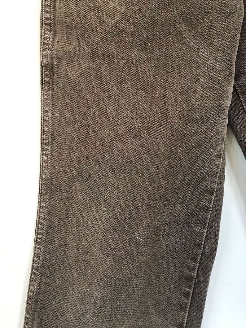 May include: Close-up of the fabric texture of a pair of brown denim jeans.