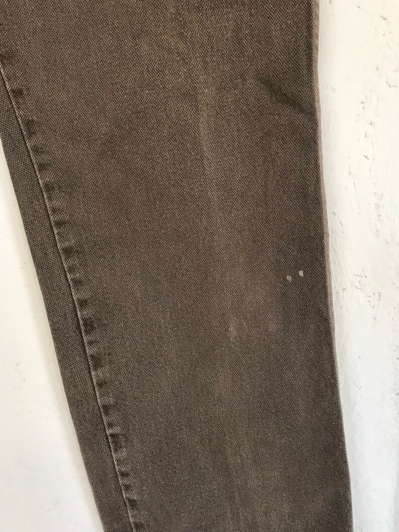 May include: Close-up of a brown pair of pants with a subtle texture. The fabric appears to be denim.