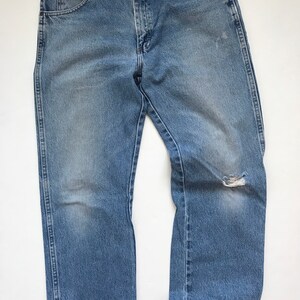 Pu&ograve; includere: Un paio di jeans in denim blu chiaro con un piccolo buco sul ginocchio destro.