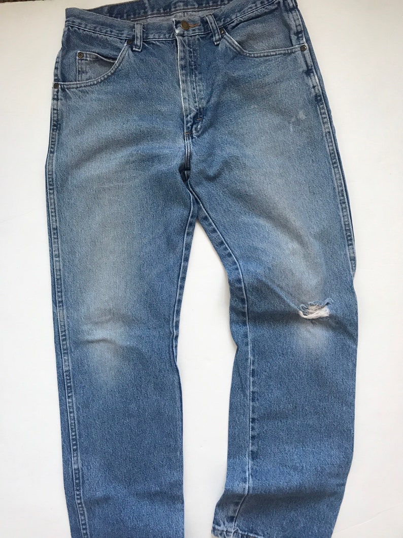 Pu&ograve; includere: Un paio di jeans in denim blu chiaro con un piccolo buco sul ginocchio destro.