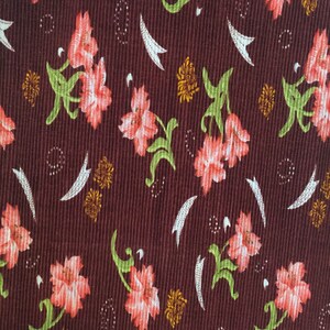 May include: A brown fabric with a repeating pattern of pink flowers and green leaves. The fabric has a textured, corduroy-like surface.