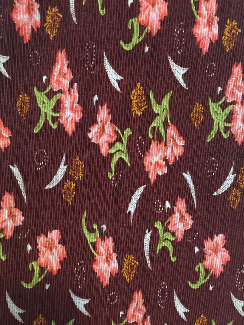May include: A brown fabric with a repeating pattern of pink flowers and green leaves. The fabric has a textured, corduroy-like surface.