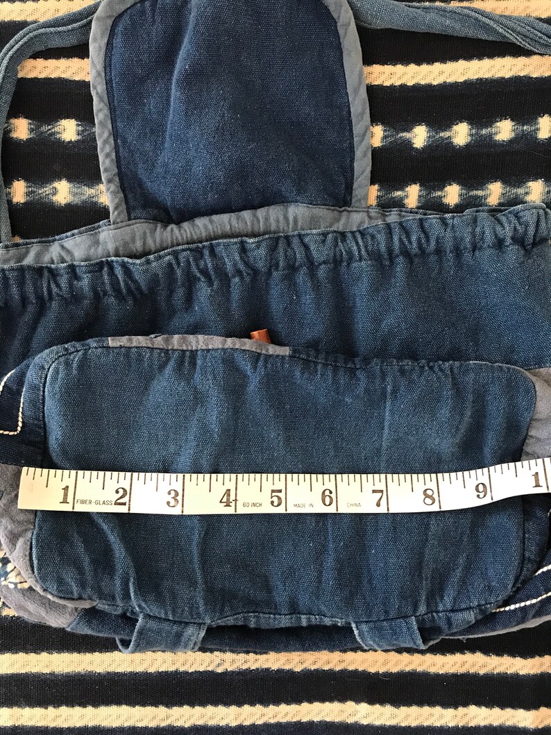 Puede incluir: Una bolsa de lona azul de mezclilla con una solapa y un cierre de cord&oacute;n. La bolsa est&aacute; hecha de diferentes tonos de mezclilla azul y tiene una cinta m&eacute;trica blanca en la parte inferior. La cinta dice "1 2 FIBER-GLASS 3 4 60 INCH 5 MADE IN 6 CHNA 7 8 9 1".