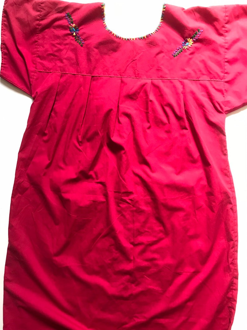 May include: A red cotton dress with embroidered floral details around the neckline. The dress has short sleeves and a loose fit.