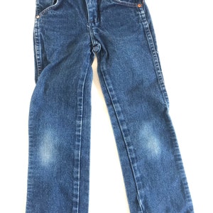 May include: Blue denim jeans with a classic five-pocket design. The jeans have a button and zipper closure, copper rivets, and a faded appearance on the knees. The jeans are designed for children.