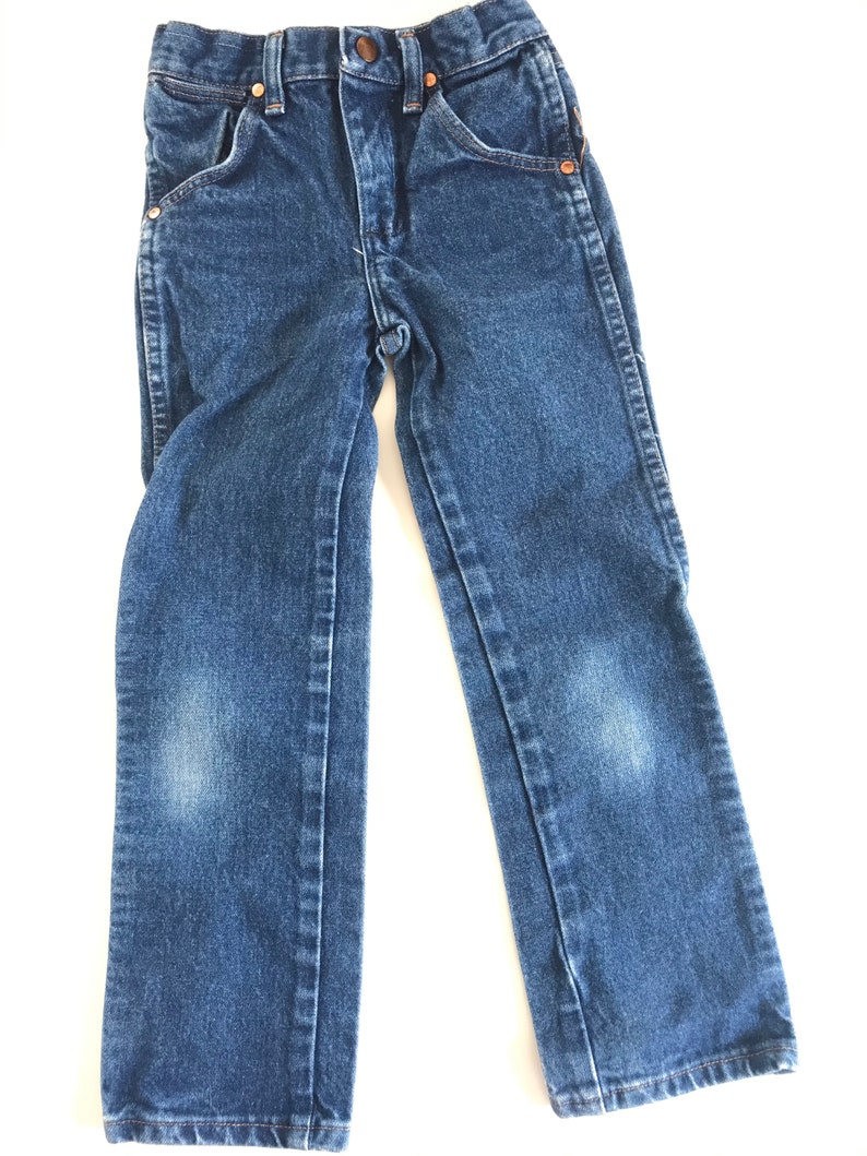 May include: Blue denim jeans with a classic five-pocket design. The jeans have a button and zipper closure, copper rivets, and a faded appearance on the knees. The jeans are designed for children.