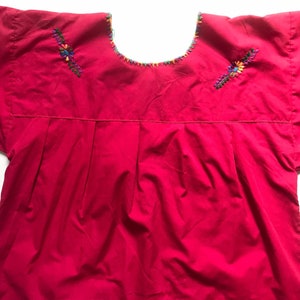May include: A bright pink cotton blouse with short sleeves and colourful embroidered floral designs on the shoulders.