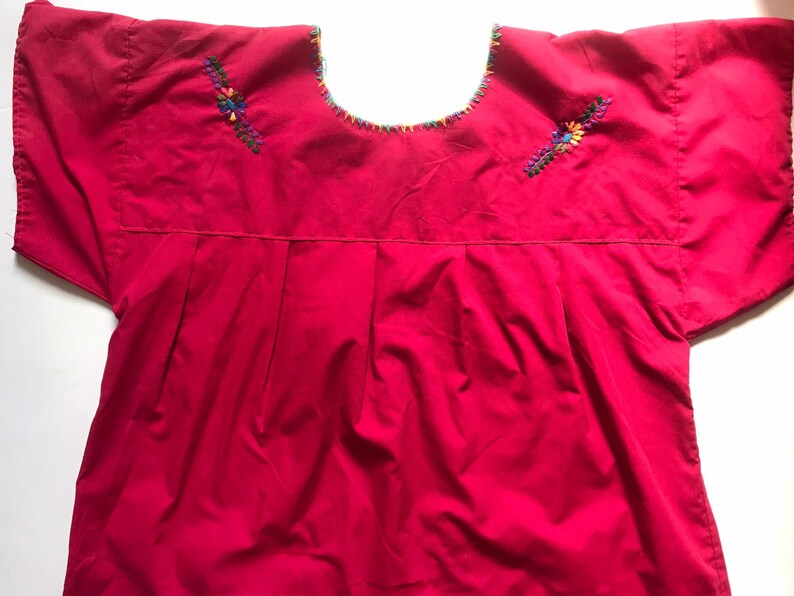 May include: A bright pink cotton blouse with short sleeves and colourful embroidered floral designs on the shoulders.