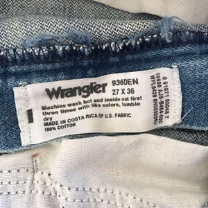 May include: A white tag with black text that reads "Wrangler 936DEN 27 X 36". The tag also includes instructions for washing the jeans: "Machine wash hot and inside out first three times with like colors, tumble dry. Made in Costa Rica of U.S. Fabric 100% Cotton."