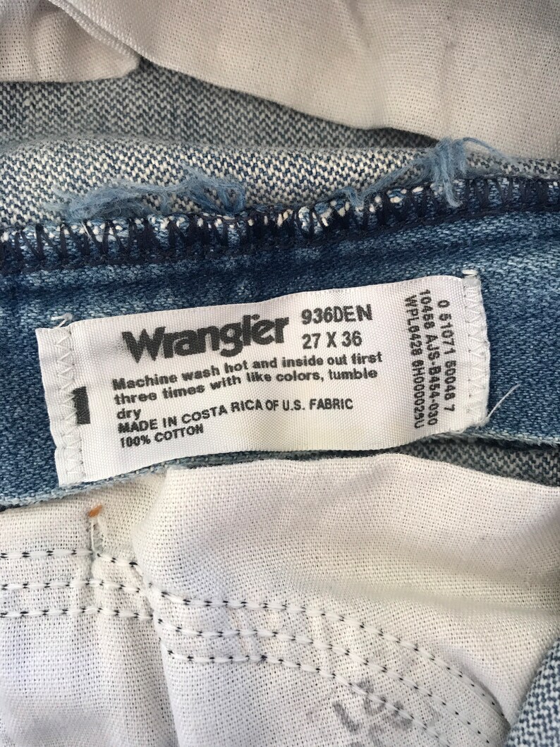 May include: A white tag with black text that reads "Wrangler 936DEN 27 X 36". The tag also includes instructions for washing the jeans: "Machine wash hot and inside out first three times with like colors, tumble dry. Made in Costa Rica of U.S. Fabric 100% Cotton."