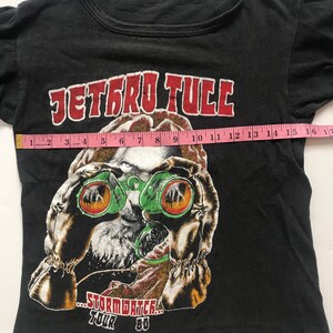 May include: Black t-shirt with a graphic of a person wearing green binoculars and the text "Jethro Tull...Stormwatch...Tour 80".