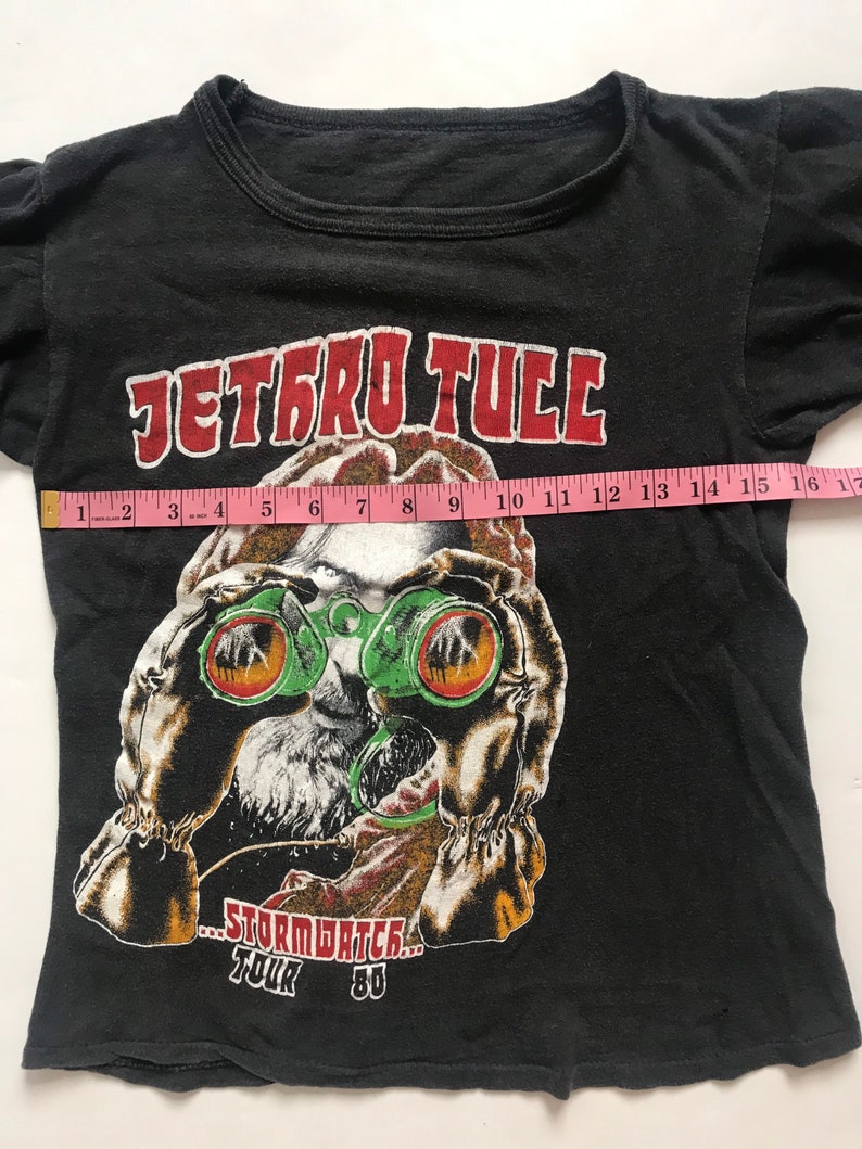 May include: Black t-shirt with a graphic of a person wearing green binoculars and the text "Jethro Tull...Stormwatch...Tour 80".