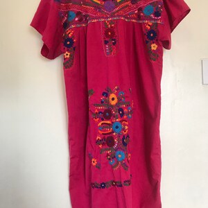 May include: A pink cotton dress with colourful floral embroidery. The embroidery is detailed and intricate, featuring a variety of flowers and leaves.