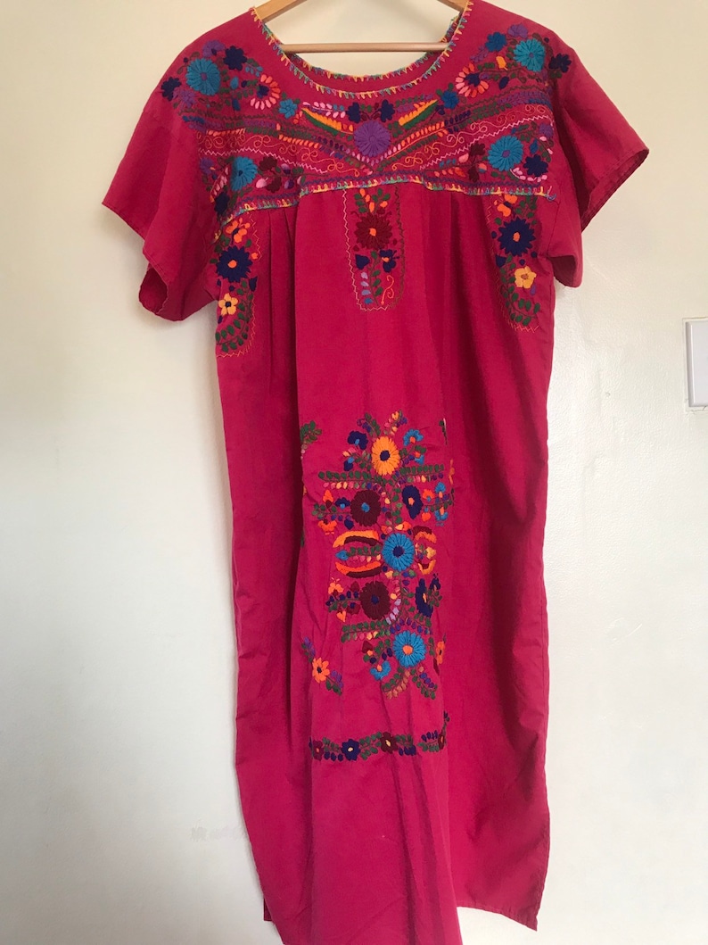 May include: A pink cotton dress with colourful floral embroidery. The embroidery is detailed and intricate, featuring a variety of flowers and leaves.