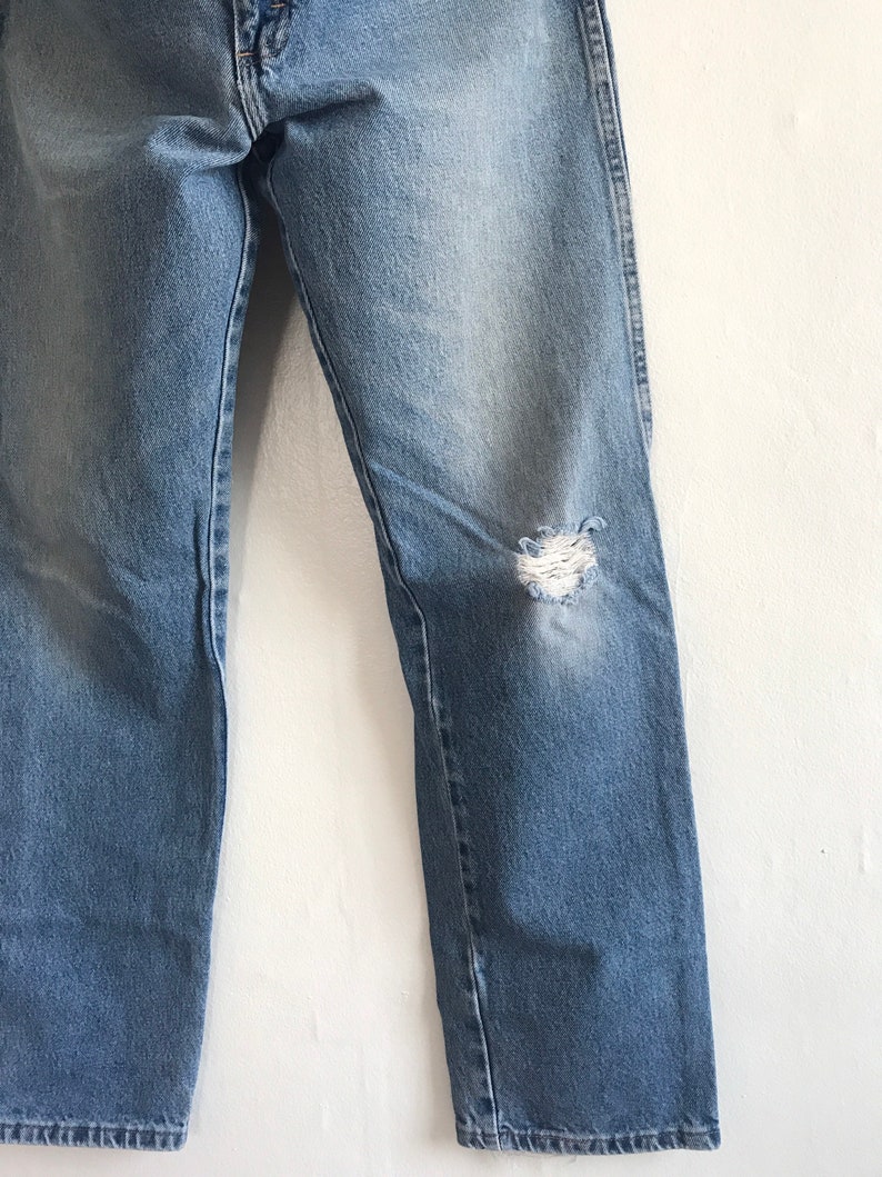 Pu&ograve; includere: Un paio di jeans in denim blu chiaro con un ginocchio consumato. I jeans hanno una gamba dritta e una vestibilit&agrave; classica.