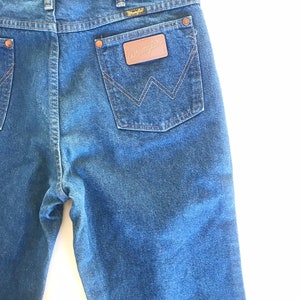 May include: A pair of blue denim jeans with a brown leather patch on the back pocket that says "Wrangler".
