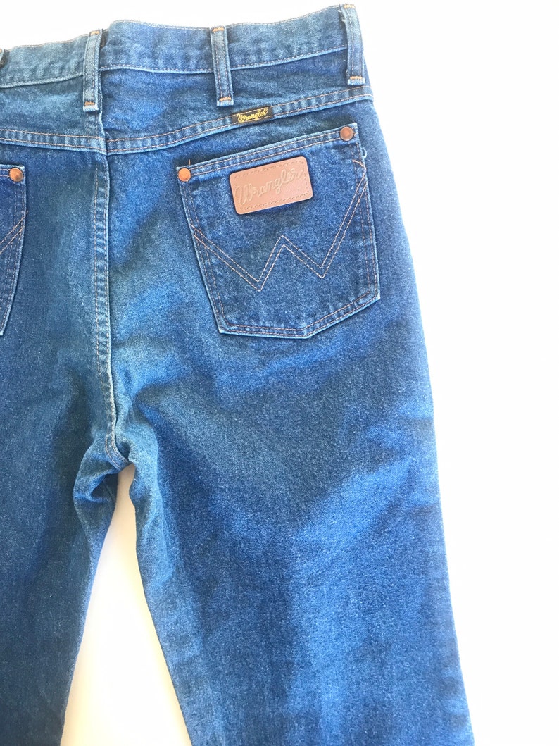 May include: A pair of blue denim jeans with a brown leather patch on the back pocket that says "Wrangler".