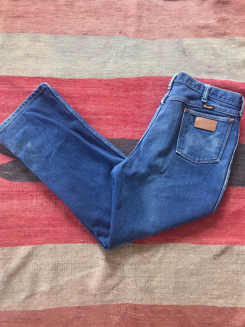 May include: A pair of blue denim jeans with a brown leather patch on the back pocket that says "Wrangler".