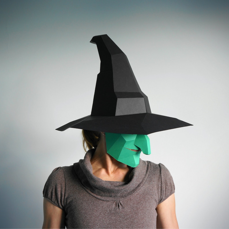K&ouml;nnte beinhalten: Eine Person tr&auml;gt einen schwarzen Hexenhut und eine gr&uuml;ne Hexenmaske. Der Hut ist spitz und hat einen breiten Rand. Die Maske ist aus Papier und hat eine spitze Nase und ein breites Grinsen.