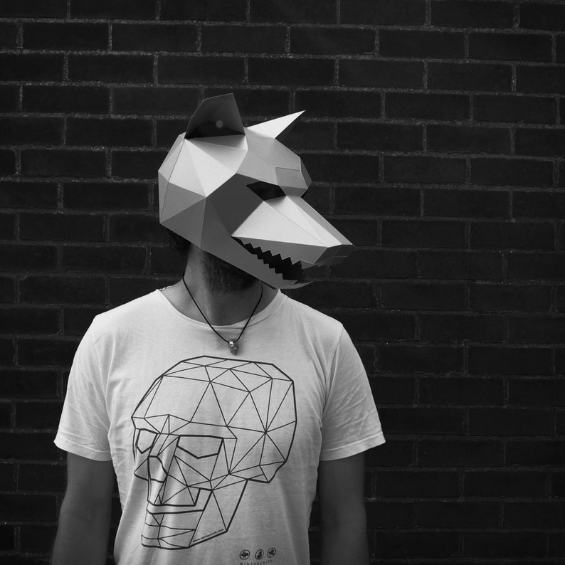 以下が含まれることがあります： 幾何学的な頭蓋骨のデザインが施された白いTシャツと、紙製の狼のマスクを着用した人物