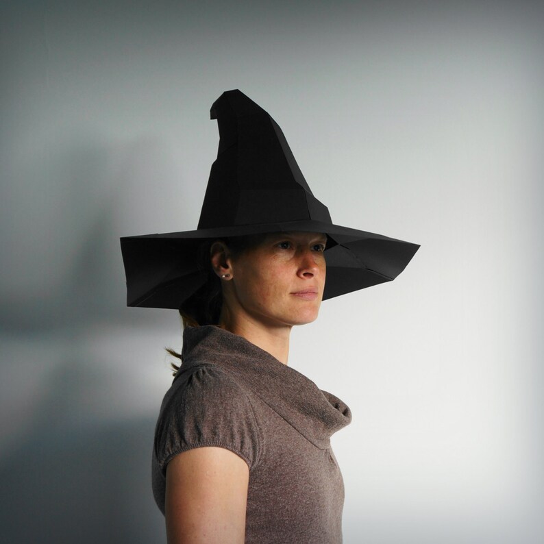 K&ouml;nnte beinhalten: Eine Person tr&auml;gt einen schwarzen Hexenhut mit breiter Krempe und spitzer Krone. Der Hut ist aus Papier und hat ein schlichtes Design.