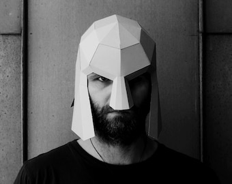 Puede incluir: Una persona con una máscara de papel blanca que se asemeja a un casco. La máscara tiene un diseño geométrico y cubre la cara de la persona desde la frente hasta la barbilla.