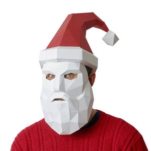 May include: A white paper Santa Claus mask with a red and white paper hat. The mask has a white beard and moustache, and the eyes are cut out.