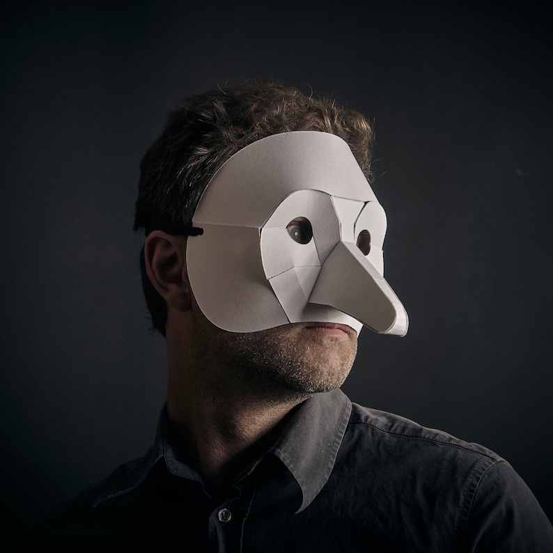 May include: A person wearing a white paper mask with a long nose. The mask is covering the person's eyes and nose. The person is wearing a dark shirt.