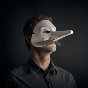 May include: A person wearing a white paper mask with a long nose and a black moustache. The mask is covering the person's face and the person is looking to the right.