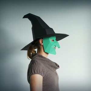 K&ouml;nnte beinhalten: Eine Person tr&auml;gt einen schwarzen Hexenhut und eine gr&uuml;ne Papiermaske mit einer langen Nase. Die Maske ist ein 3D-Design und hat ein spitzes Kinn.