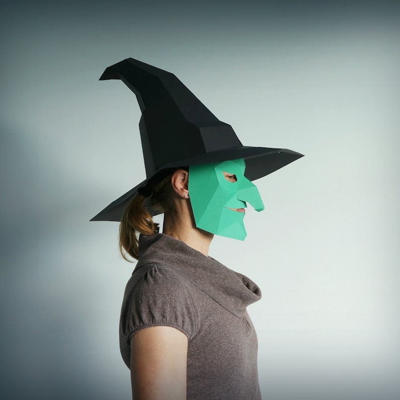 K&ouml;nnte beinhalten: Eine Person tr&auml;gt einen schwarzen Hexenhut und eine gr&uuml;ne Papiermaske mit einer langen Nase. Die Maske ist ein 3D-Design und hat ein spitzes Kinn.