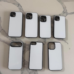 May include: A collection of seven rectangular phone cases with white back panels and black borders. The cases feature various camera cutout configurations, including circular and square shapes, arranged in two rows on a light surface.