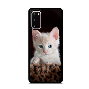 Op de afbeelding: Zwarte telefoonhoes met een close-up van een lichtgekleurd katje met helderblauwe ogen. Het katje ligt in een bruin bed met luipaardprint. De telefoonhoes heeft een zwarte rand en een cameramodule.