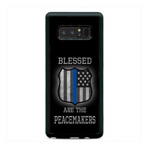May include: Black phone case featuring a shield design with a blue stripe and American flag stars. The text "BLESSED ARE THE PEACEMAKERS" is displayed in white. The case is designed to fit a smartphone.