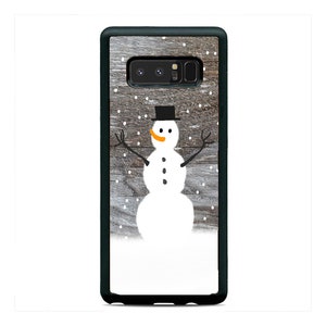 May include: A black phone case with a woodgrain background and a white snowman illustration. The snowman has a black top hat, orange carrot nose, and black eyes and buttons.