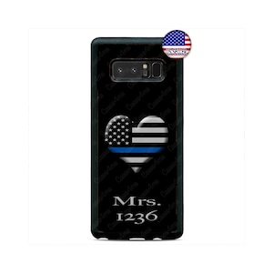 May include: A black phone case with a thin blue line heart design and an American flag in the top left corner. The text "Mrs. 1236" is printed in silver below the heart.