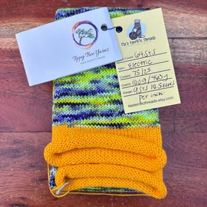 May include: A skein of hand-dyed yarn in a mix of yellow, blue, and green, with a bright yellow cuff. The yarn is labelled "Electric" and "Tippy Tree Yarns, hand dyed in Colorado". A tag provides details about the yarn's content and gauge.