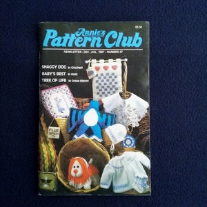 May include: A vintage issue of Annie's Pattern Club newsletter, featuring various crochet and knit projects. The cover displays a variety of handmade items, including a shaggy dog, baby clothes, and cross-stitch designs. The newsletter is dated December-January 1987.