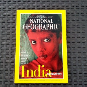 May include: A May 1997 issue of National Geographic magazine featuring a cover image of a person with red skin. The magazine has a yellow border and the title "India" in large yellow letters.