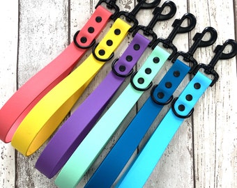 Op de afbeelding: Zes kleurrijke hondenriemen met zwarte metalen clips. De riemen zijn in tinten roze, geel, paars, lichtblauw, turquoise en blauw.