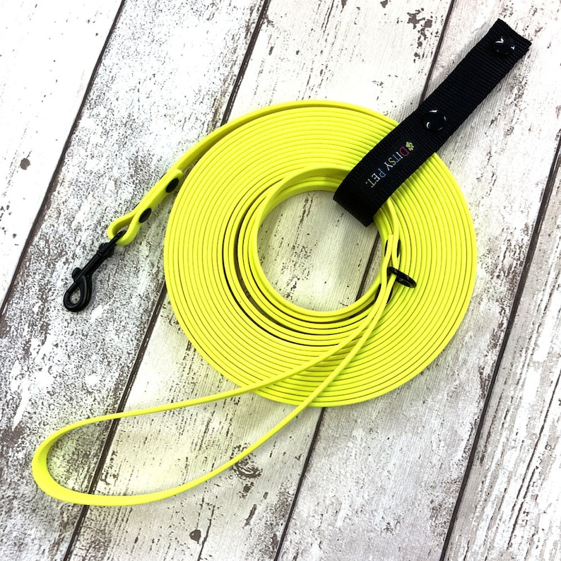 May include: A coiled bright yellow dog lead with a black clip and a black handle. The handle features the text "DITSY PET." The lead is made of a flexible, durable material and is shown on a wooden surface.