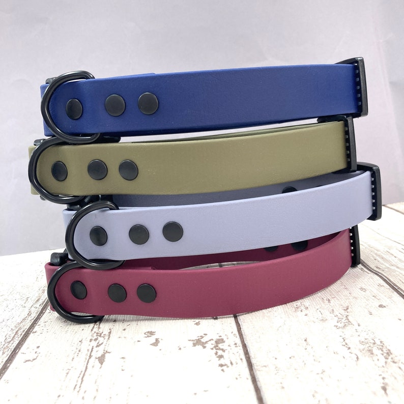 May include: Four dog collars stacked on top of each other. The collars are made of a soft, flexible material and have a black buckle and black metal accents. The collars are in the colours blue, green, light blue, and burgundy.