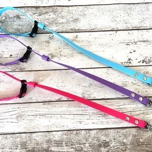 Pode incluir: Três trelas para cães em cores diferentes: azul claro, roxo e rosa. Cada trela tem um clipe de metal em uma extremidade e um colar ajustável preto na outra.