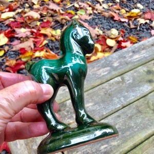 May include: A green ceramic horse figurine with a glossy finish. The figurine is standing on a wooden surface.