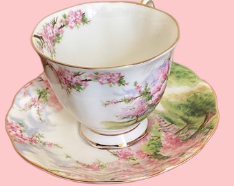 May include: A white teacup and saucer with a floral pattern of pink and green flowers. The cup and saucer have a gold trim.