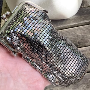 May include: A small, rectangular coin purse crafted from silver-toned metal mesh. The purse features a hinged metal frame with a dual-ball clasp closure at the top. The flexible mesh material has a reflective, shimmering surface texture.